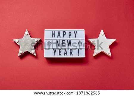 New Year or Christmas composition, flat lay, top view. Light box inscription Happy New Year and wooden decorations of stars on red.