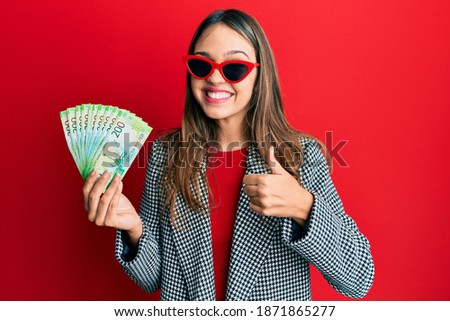 Young brunette woman holding russian 200 ruble banknotes smiling happy and positive, thumb up doing excellent and approval sign 
