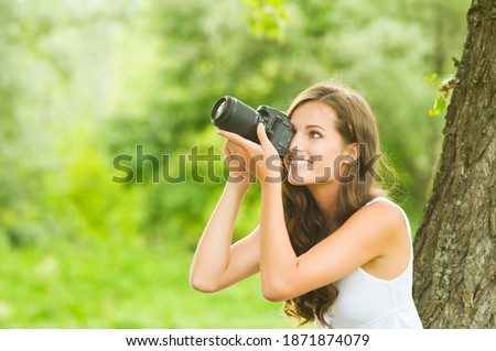 Beautiful smiling woman is professional photographer with DSLR camera and taking pictures outdoors in summer nature.