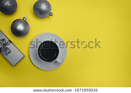 Cup of espresso coffee, gift box and gray Christmas balls on a yellow background. Flatlay. View from above. Colors of the year 2021.