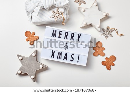 New Year or Christmas composition, flat lay, top view. Light box inscription Merry Christmas, gifts in Japanese furoshiki style and gingerbread cookies, copy space.