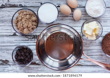 Top view of ingredients for homemade fudgy brownies and sauce pan over a white rustic wooden table. 