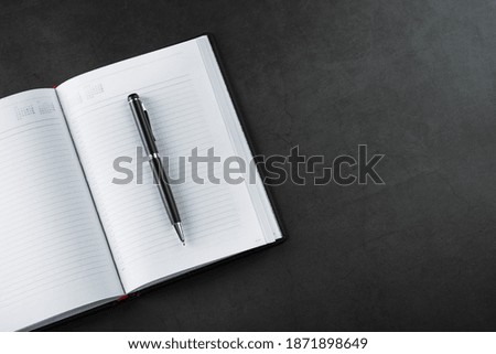 An open Notebook with a black pen on a black background.