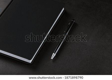 Office desk with black notepad and pen on black background.
