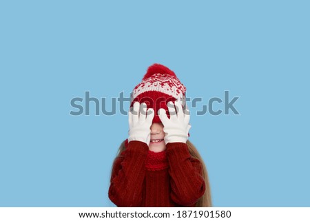 Winter portrait of happy child girl wearing knitted red hat, snood and sweater. Wow face. Blue background. childrens winter entertainment