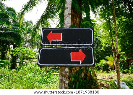 The signpost is made of wood, painted in black, with a red arrow pointing to the left, and a red arrow pointing to the right. Suitable as a sign for directions in getting to a place or meeting point.