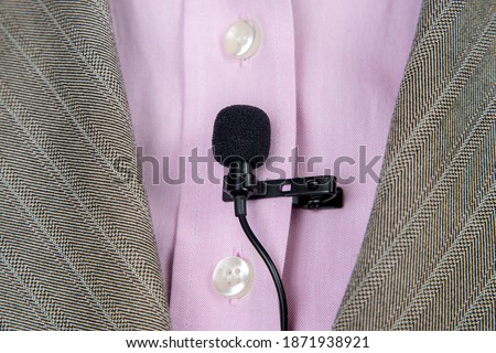 The lavalier microphone is secured with a clip on a women's shirt close-up. Audio recording of the sound of the voice on a condenser microphone.