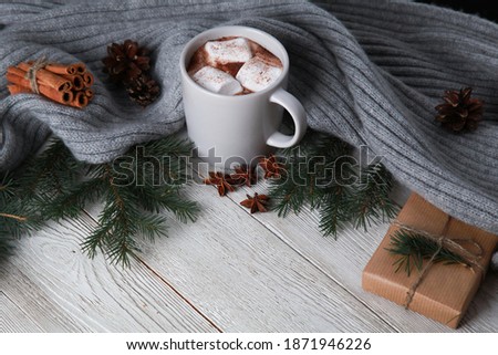Mug of cocoa, knitted plaid, fir tree branches, cones, craft gift wrap on white wooden table. Winter and Christmas concept. Spicy cocoa, New Year, closeup, copy space