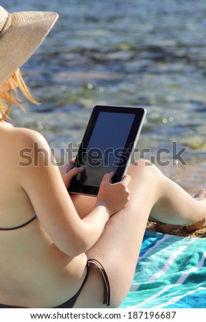 Back view of a woman reading a tablet on vacations on the beach