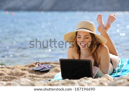Woman on the beach browsing social media on a computer in summer with the sea in the background             