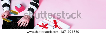 Hands holding credit card in front of laptop with gifts on pink background banner space. Concept of online shopping