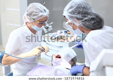 The dentist and assistant perform professional dental cleaning for the patient. Protective screen and medical mask on the face. Binocular glasses. The concept of health. Top view.