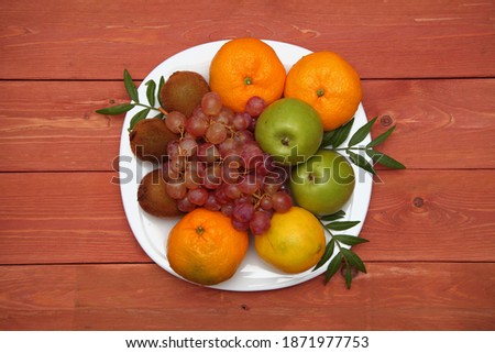 Fruit concept. Kiwi, bunch of grapes, orange, green apple on a white plate. on wooden background