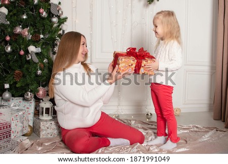 Merry Christmas and Happy Holidays. Cheerful mom and her cute daughter girl exchanging gifts. Parent and little child having fun near Christmas tree indoors. Loving family with presents in room.