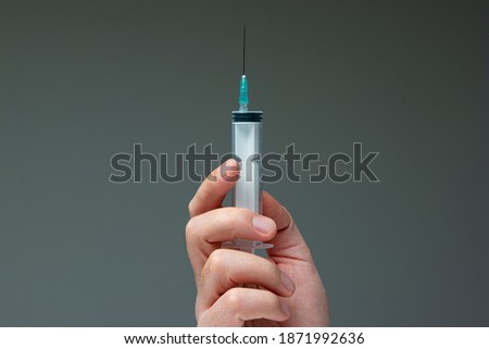Caucasian male hand holding a large syringe with needle  close up shot isolated on gray.