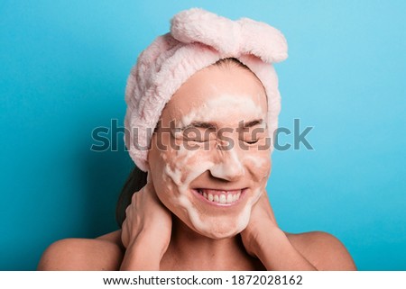 Beautiful happy young woman with cosmetic foam in her face wearing a pink turban after having a shower