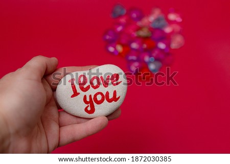stone in shape of heart with inscription I love you written in hand paints on female palm on red background with glass decor