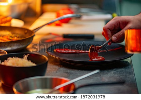Adding red sauce on a black plate, side view, close-up. Food decoration concept.