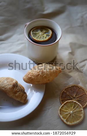 on craft paper there is a white dish on which there are two sweet tasty croissants and a white cup with tea and lemon next to it. for banners, labels, splash screens, business cards, recipe flyers