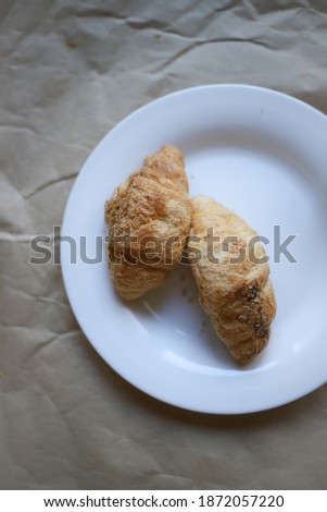 on craft paper there is a white dish on which lies two sweet tasty croissants. for banners, labels, splash screens, business cards, recipe flyers
