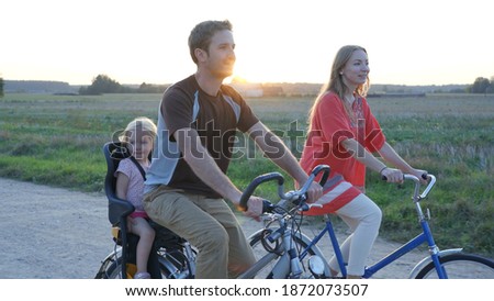 Young couple on a bike with their little daughter at sunset.