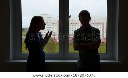 Quarantine concept. Silhouette of young spouses swearing on the background of the window of their apartment.