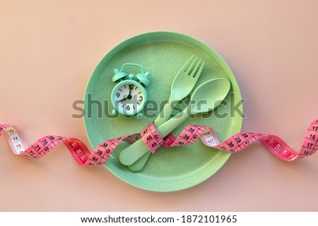 Creative flat lay composition with plate, alarm clock, spoon, fork and measuring tape on pink background. Intermittent fasting, ketogenic, diet concept.  Flat lay, copy space.
 Royalty-Free Stock Photo #1872101965