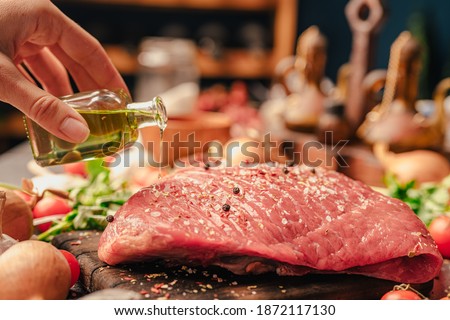 Woman's hand seasoning with extra virgin olive oil and spices a veal round cut meat for a dinner roast. Preparing a large portion of meat for a group of people.Protein based diet. Dinner party roast Royalty-Free Stock Photo #1872117130