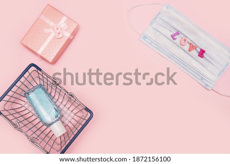 Medical protective mask, pink gift box, antiseptic hand gel in a shopping basket on a pink background. Valentine's day gifts in the age of coronavirus. Concept of sales, purchases and discounts.