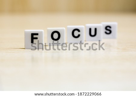 A row of small white plastic tiles, containing the letters forming the word focus, torepresents the concept of visually focusing or a topic.