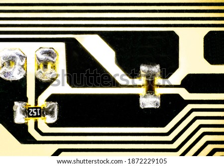 The macro photo of a small part of an electric circuit colored in yellow and black, with components soldered on it, which emits yellow light thanks to the backlight.