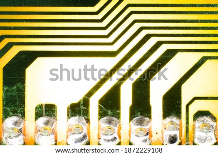 The macro photo of a small part of an electric circuit colored in yellow and green, which gives off yellow light thanks to the backlight.