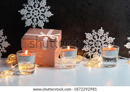 Beautiful composition of golden rose gift box with shiny bow for present, candles, snowflakes for Christmas celebrating