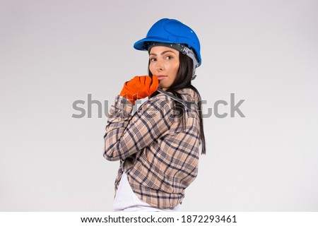 A woman mechanic in a hard hat holds a wrench on a white background looking at the camera. Side space for advertisment
