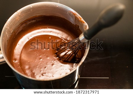 Preparing delicious hot chocolate with a whisk in a metal saucepan. Close up shot of traditional recipe, top view.