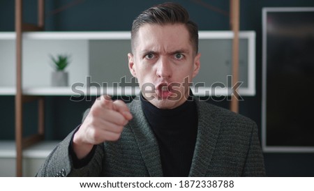Close-up angry businessman shouting and pointing at camera. Portrait of aggresive boss scolding and shouting at employees threatening with a finger and shouting at the camera. Royalty-Free Stock Photo #1872338788