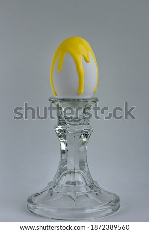 A chicken egg with illuminating yellow paint dripping in a vintage classic glass candlestick holder on a ultimate gray background. Creative minimal modern concept of Easter, color of the year 2021.