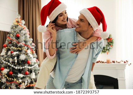 Happy couple in Santa hats near Christmas tree at home