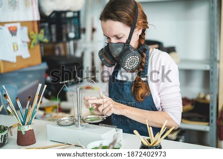 Caucasian woman mixing painting colors with a vintage balance inside her creative pottery studio - Focus on her eye