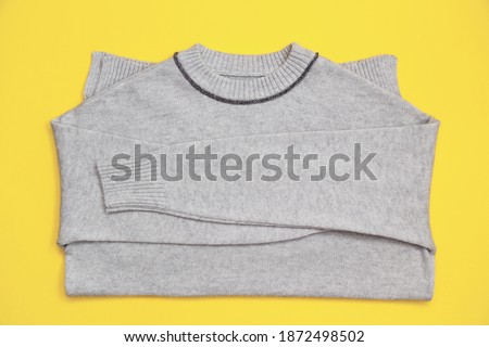 Knitted pullover in trendy grey color on a yellow background in flay lay style. Color of the 2021 year 17-5104 Ultimate Gray and 13-0647 Illuminating.