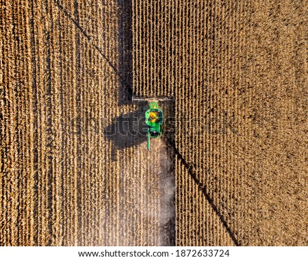 Aerial top down drone photo of green combine tractor harvester in action harvesting a field of dried corn Royalty-Free Stock Photo #1872633724