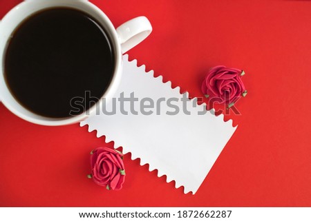 On a red background is a white sheet of paper near a Cup of coffee and roses. Holiday background with space for text.