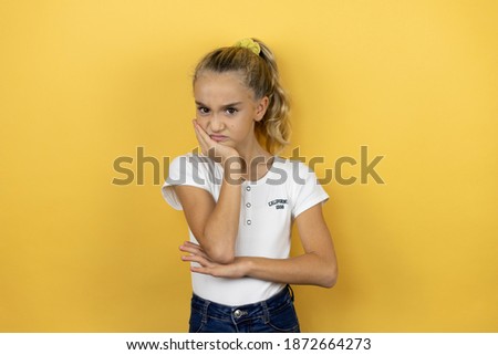 Young beautiful child girl standing over isolated yellow background thinking looking tired and bored with crossed arms