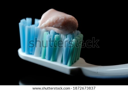 Toothbrush with light pink toothpaste on black background close-up macro photography
