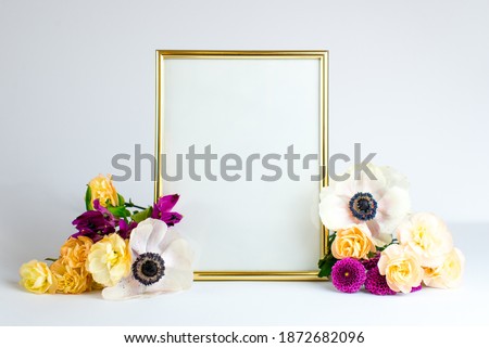 Gold empty frame with bouquet of spring flowers. Mock up frame and colorful flowers. Empty frame mock up for presentation design, modern art. Space for text. 