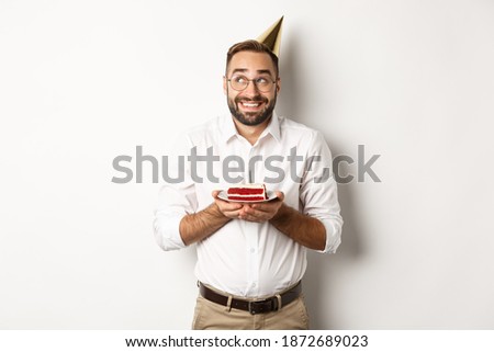 Holidays and celebration. Happy man having birthday party, making wish on b-day cake and smiling, standing against white background