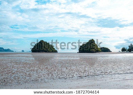 Twin islands in the middle of the blue sea ,There is little space between the islands. At low tide Revealing the rough sandy beach as the foreground of the picture.There is a bright sky background.