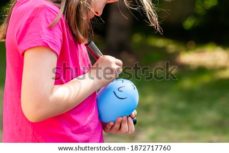 Young child, sa little girl drawing a happy smiling face on a ballon using a black marker outdoors, closeup. Children and imaginary friends, loneliness, creative arts and crafts ideas abstract concept