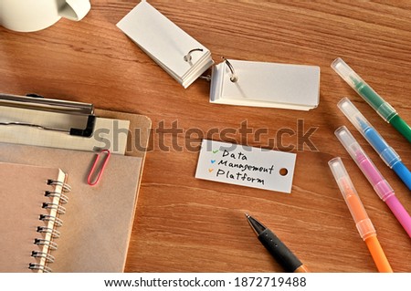 There is a a word card with Data Management Platform written on it. They are on the desk along with stationery such as notebooks and colored pens.