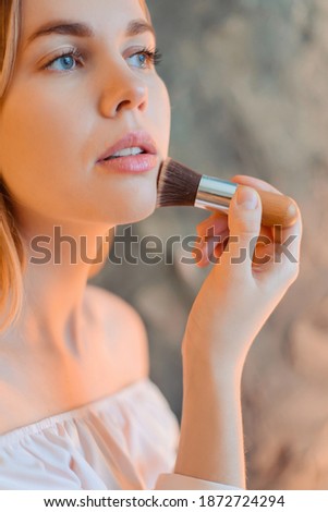 The girl does makeup. Applies powder to the face with a kabuki brush.